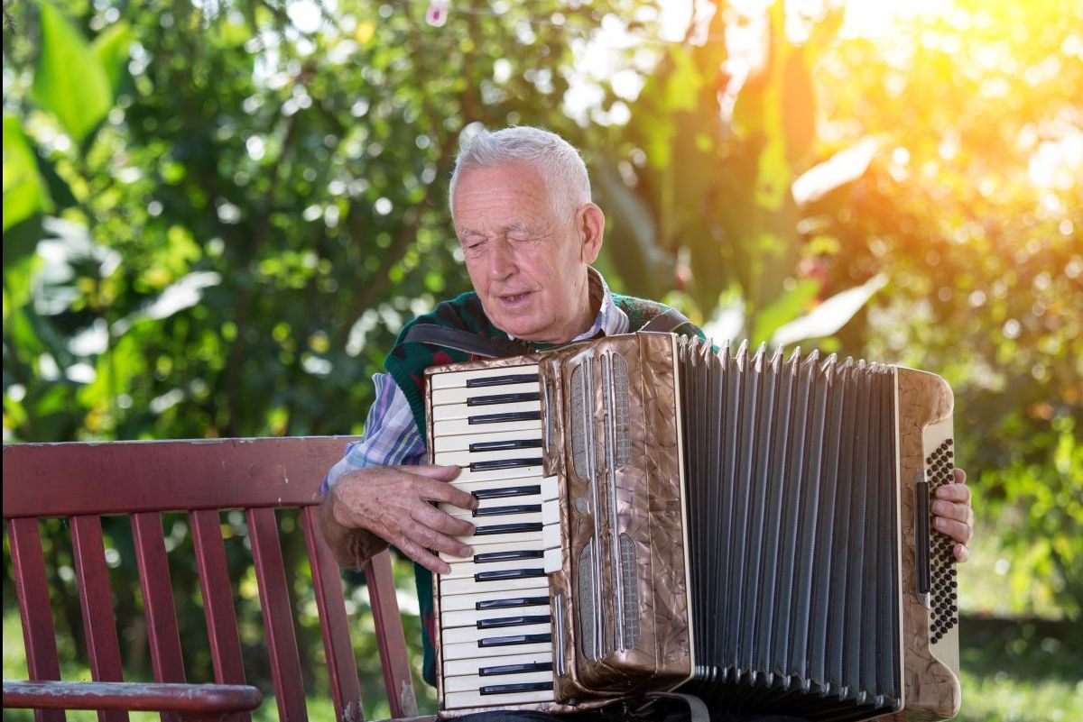 A senior man playing the accordion on a porch